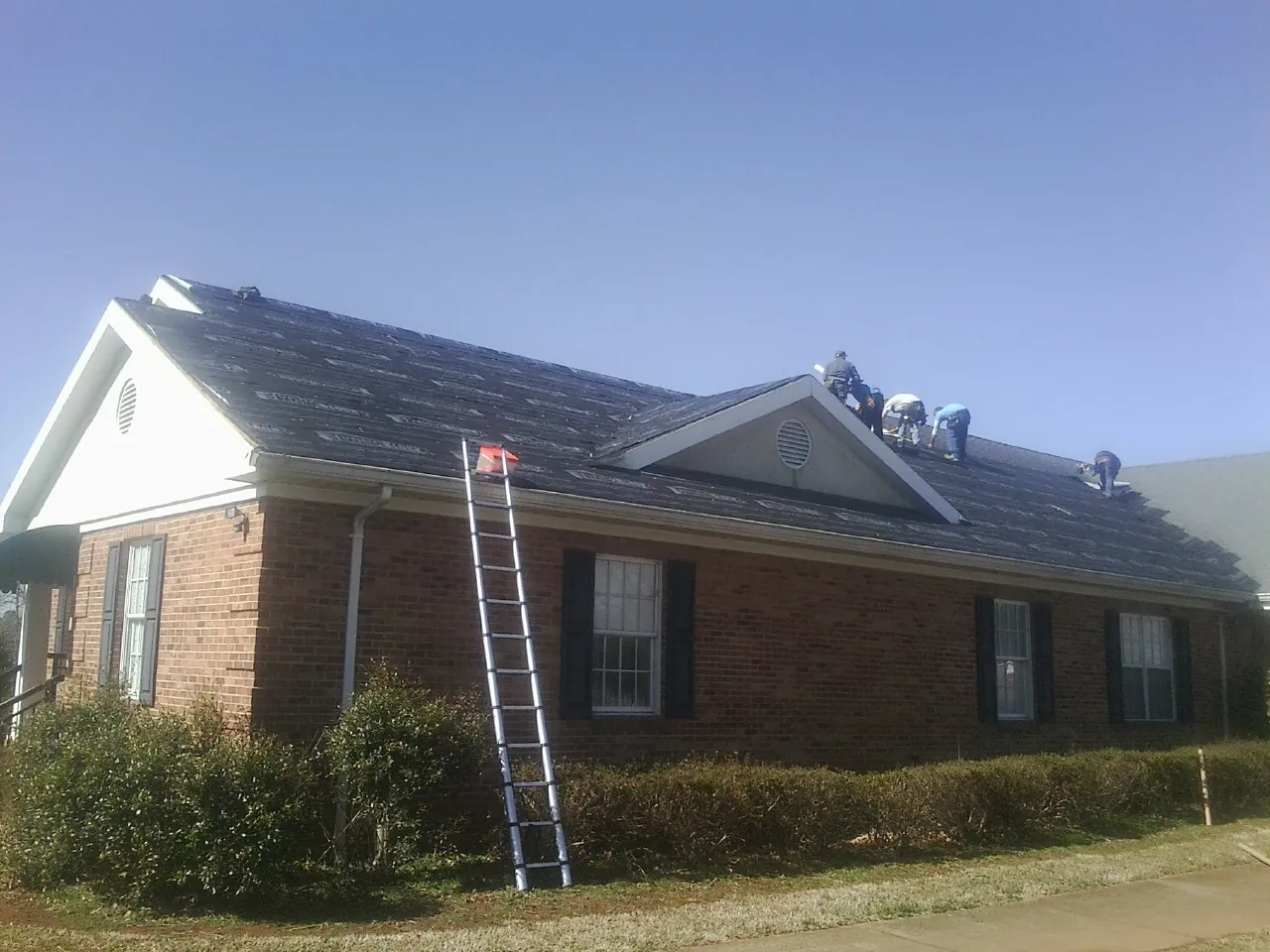 Crew tearing shingles off a brick ranch roof with a ladder set — Metal Roof Repair work by our crew in Manteca