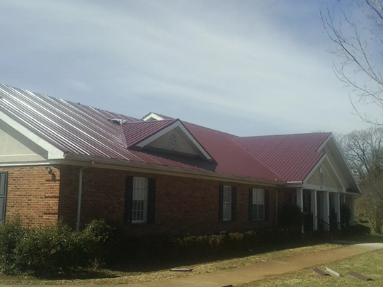 Red metal roof with gabled entries on a long brick building, from a Hail Damage Roof Repair job in Manteca