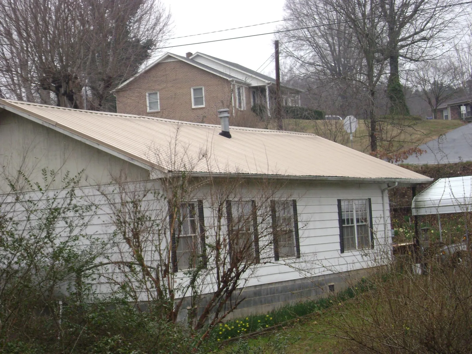Tan metal roof on a white sided house set into a hillside — Commercial Roofing by Roofing Brothers in Manteca